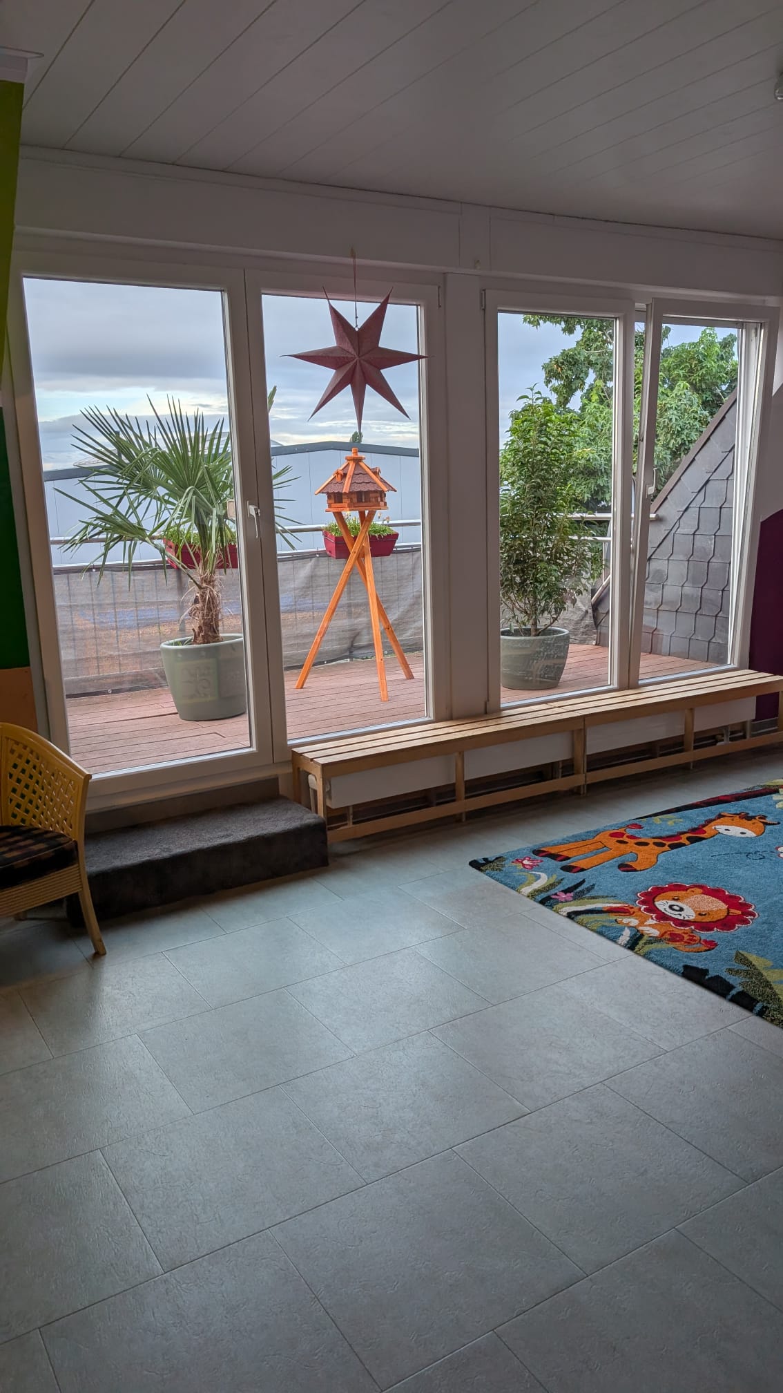 Heller Spielbereich mit großer Fensterfront, Spielteppich und Terrasse im Hintergrund